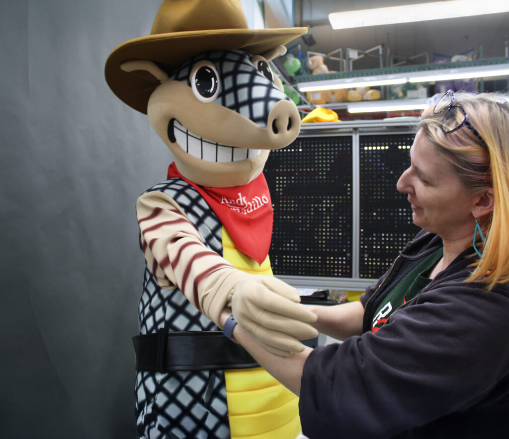 Andy Armadillo Mascot putting on costume with help.