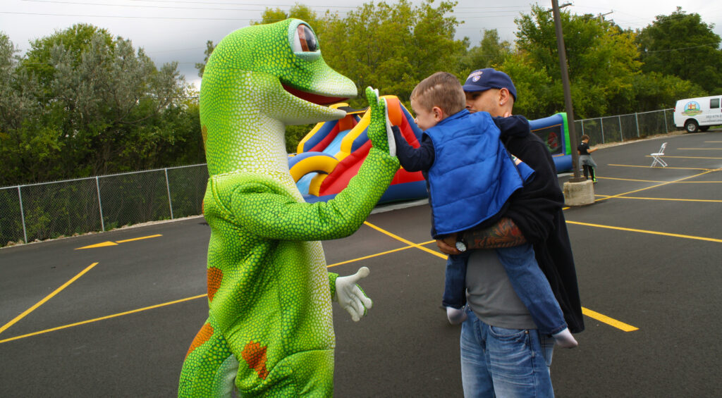 Geico Gecko Mascot giving a kid a high five.