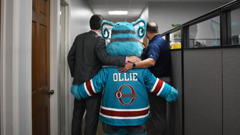 Ollie Olympus hugging two co-workers from Olympus Group.