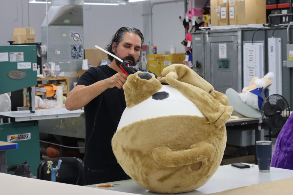 Olympus designer gluing fur on a custom mascot bear head.