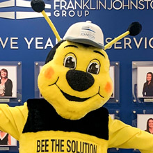 Smiling bee mascot posing in front of employee picture wall