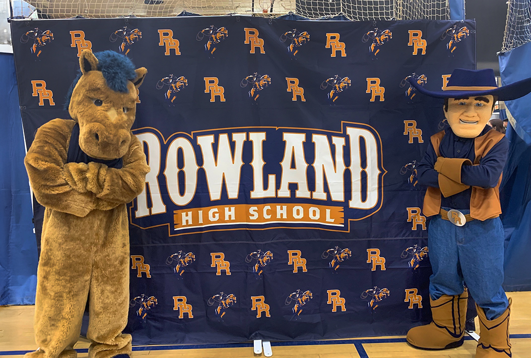Rowland High School Mascots posing in front of school banner.