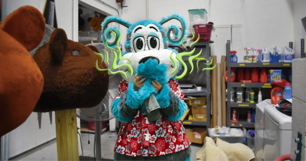 Ollie Olympus Mascot smelling his mascot hand that needs cleaning.