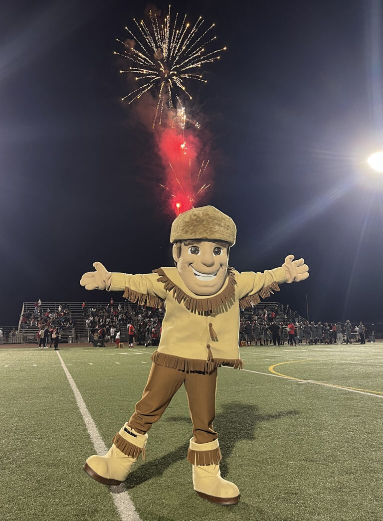 A pioneer mascot on a football field in front of a firework.