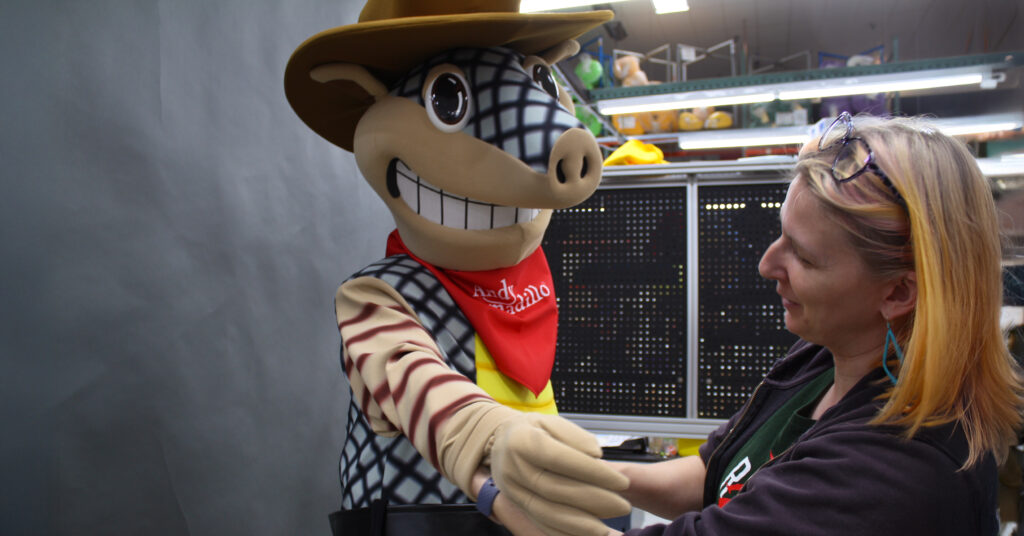 Olympus employee helping a performer put on the Andy Armadillo Mascot.